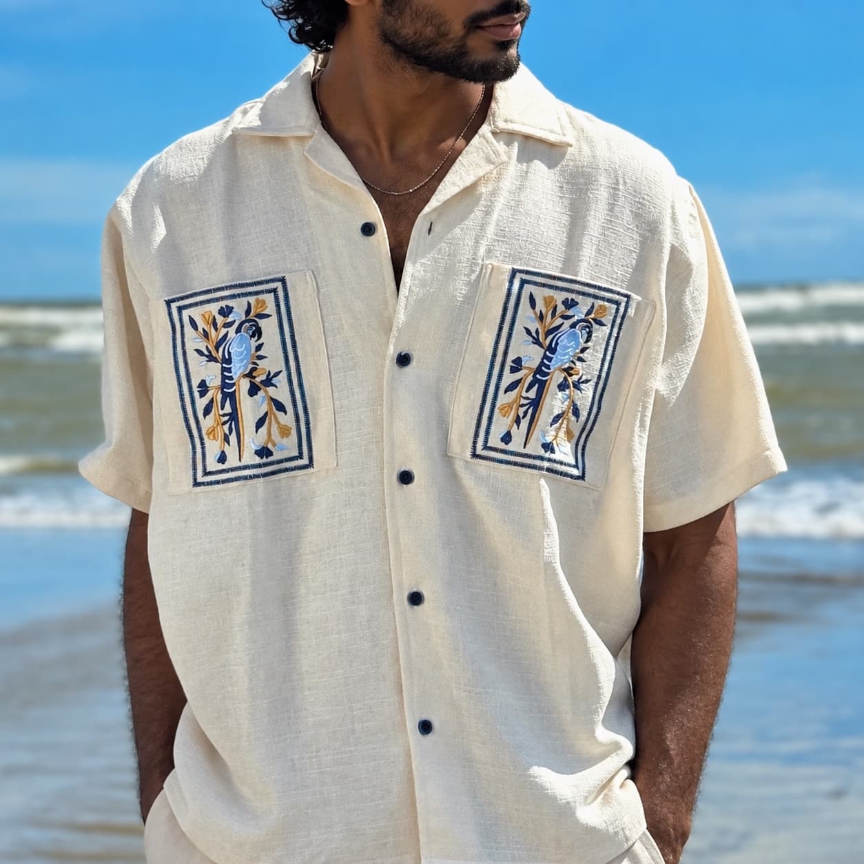 Ivory camp shirt with framed parrot embroidery on the pockets and back